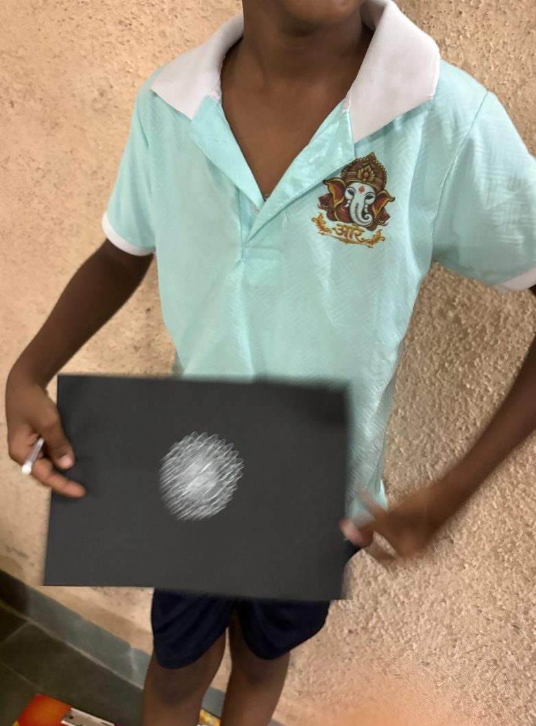 A child in school uniform holding up his completed artwork.