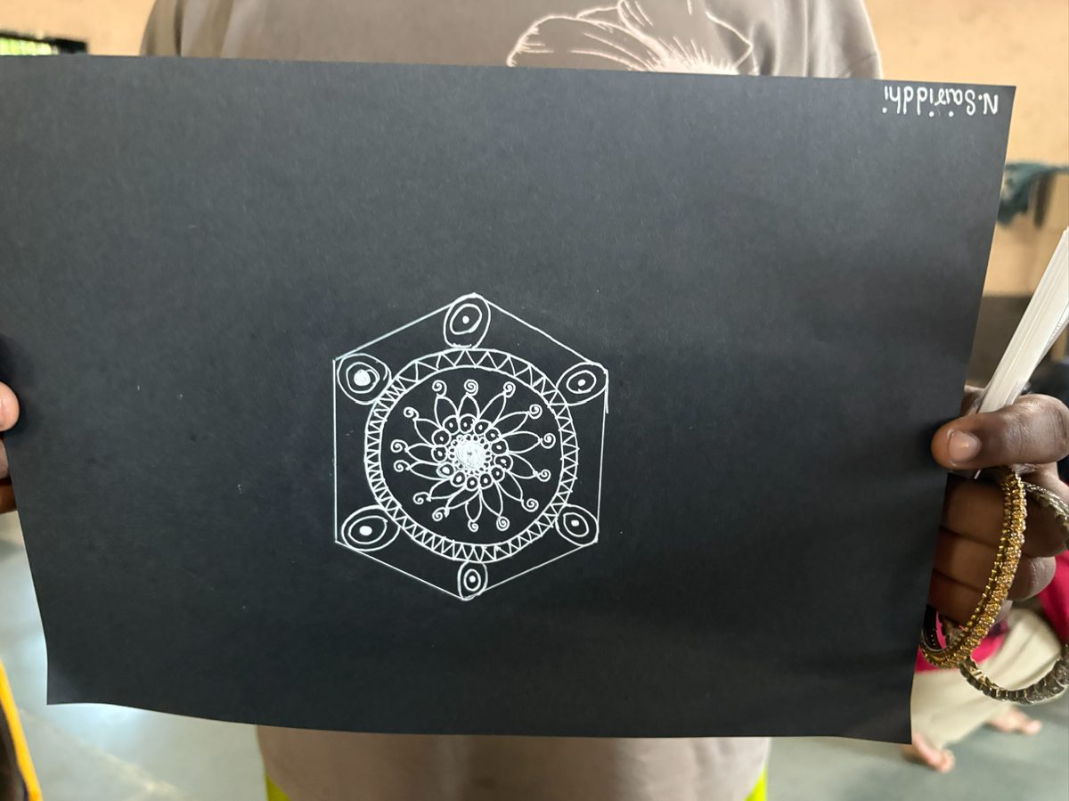 A finished white mandala drawn on black paper, held up to the camera.
