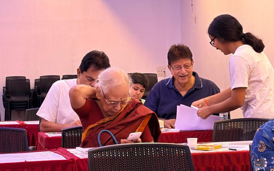 A session underway in a community hall with volunteers assisting seated participants.