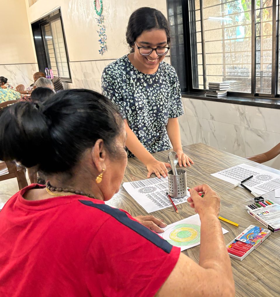 A volunteer leaning in beside a participant to help with a fine motor art task.
